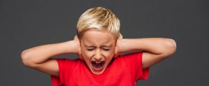 Screaming little boy child covering ears with hands.